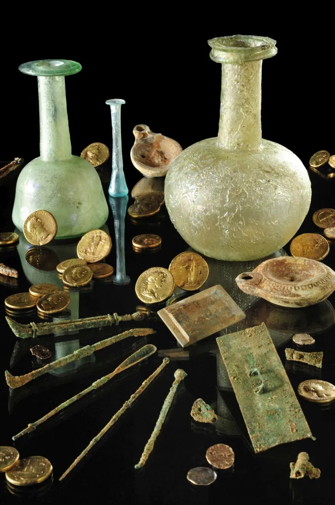 Przedmioty odkryte w gabinecie chirurga, w tym m.in.: zestaw narzędzi chirurgicznych, płytka kamienna do rozcierania substancji, dwie większe butelki  szklane i mała fiolka, lampki oliwne. Źródło: Instytut Archeologii UJ