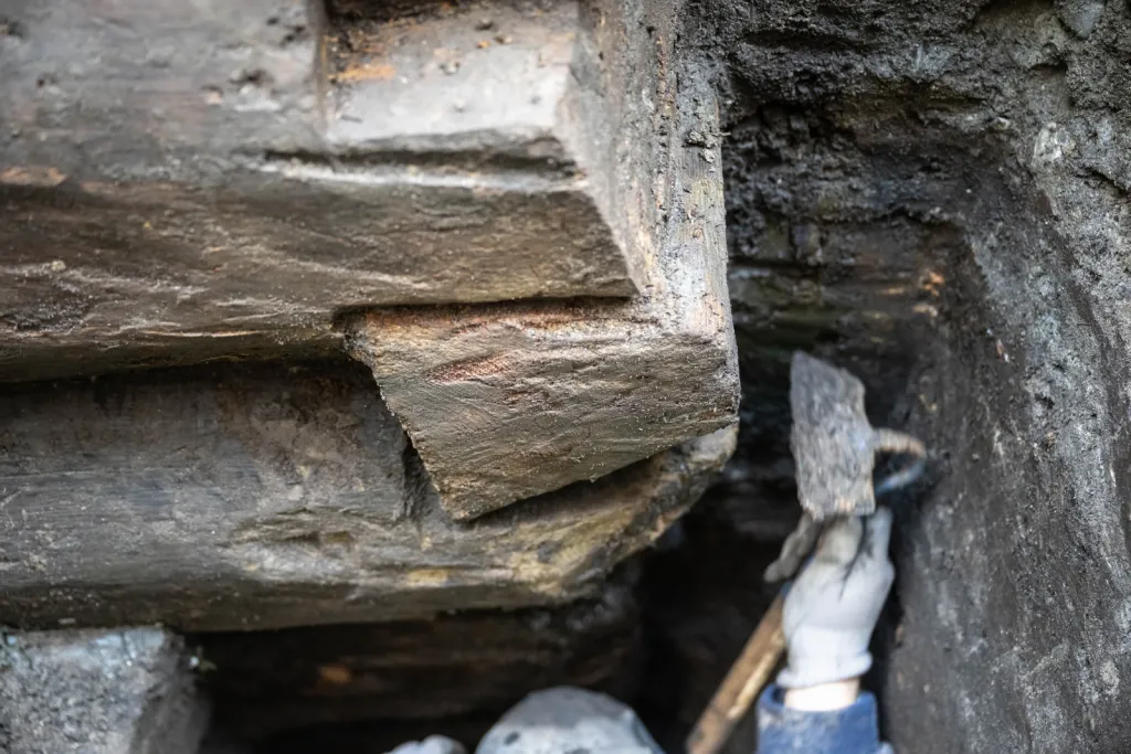 Toruń, 19.11.2025. Fragment nieznanych wcześniej drewnianych konstrukcji z XIII wieku, 19 bm. w Toruniu. Konstrukcje odkryte zostały podczas badań archelogocznych na dziedzińcu Domu Mikołaja Kopernika w Toruniu. To jedne z najstarszych takich znalezisk w mieście. Konstrukcje trafią do konserwacji i staną się elementem przyszłej wystawy stałej muzeum. (mr) PAP/Tytus Żmijewski